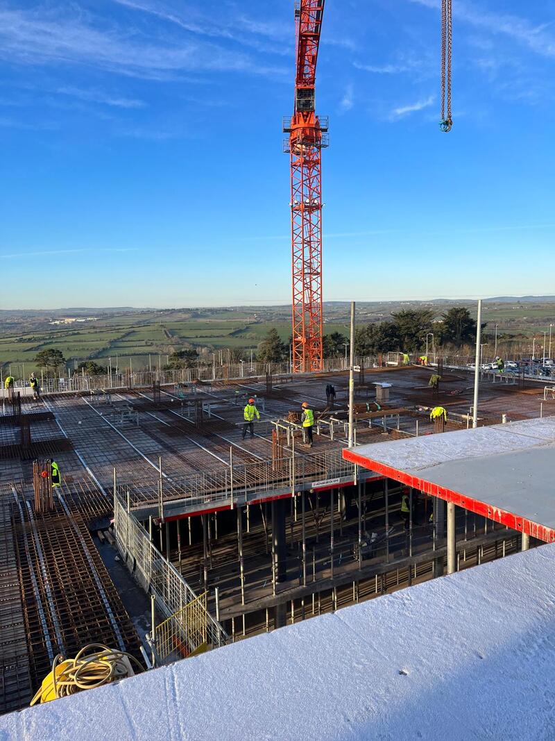 A crane and workers on top a building with steel rods being formed to pour concrete. 
